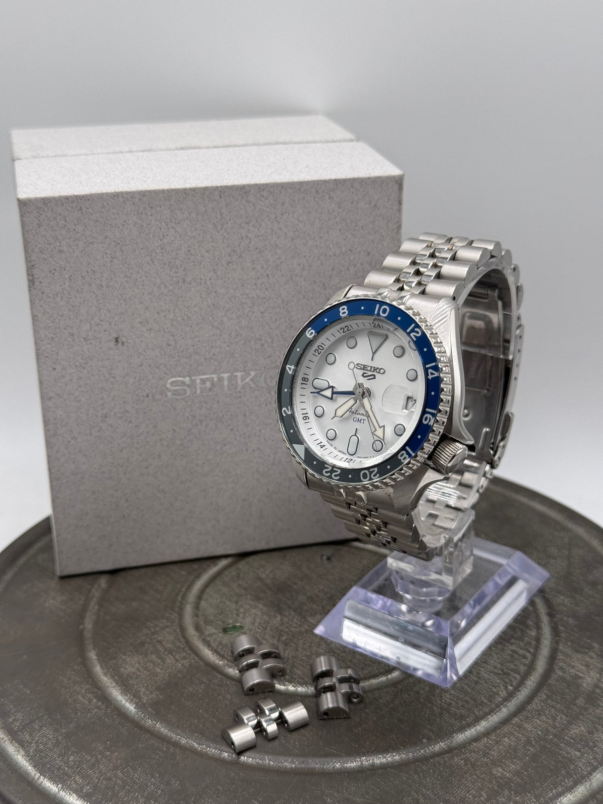 Seiko 5 Sports GMT Automatic Watch – White Dial, Blue & Black Bezel, Stainless Steel Jubilee Bracelet, with Box
